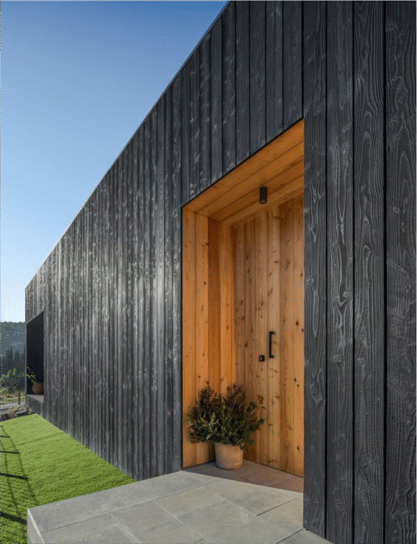 Entrada principal d’una casa moderna revestida amb fusta carbonitzada de tons foscos, en contrast amb l’interior de fusta natural clara. El disseny minimalista ressalta la textura del Yakisugi i crea un accés elegant i acollidor.