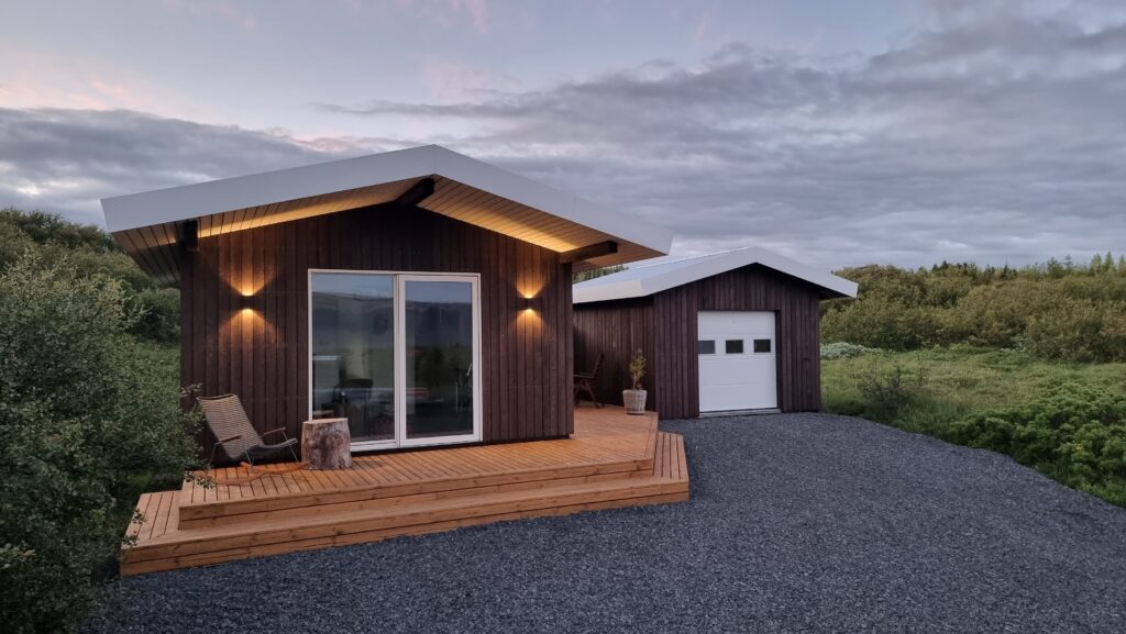Casa de madera contemporánea con fachada Yakisugi, terraza de madera natural y garaje anexo, rodeada de vegetación.