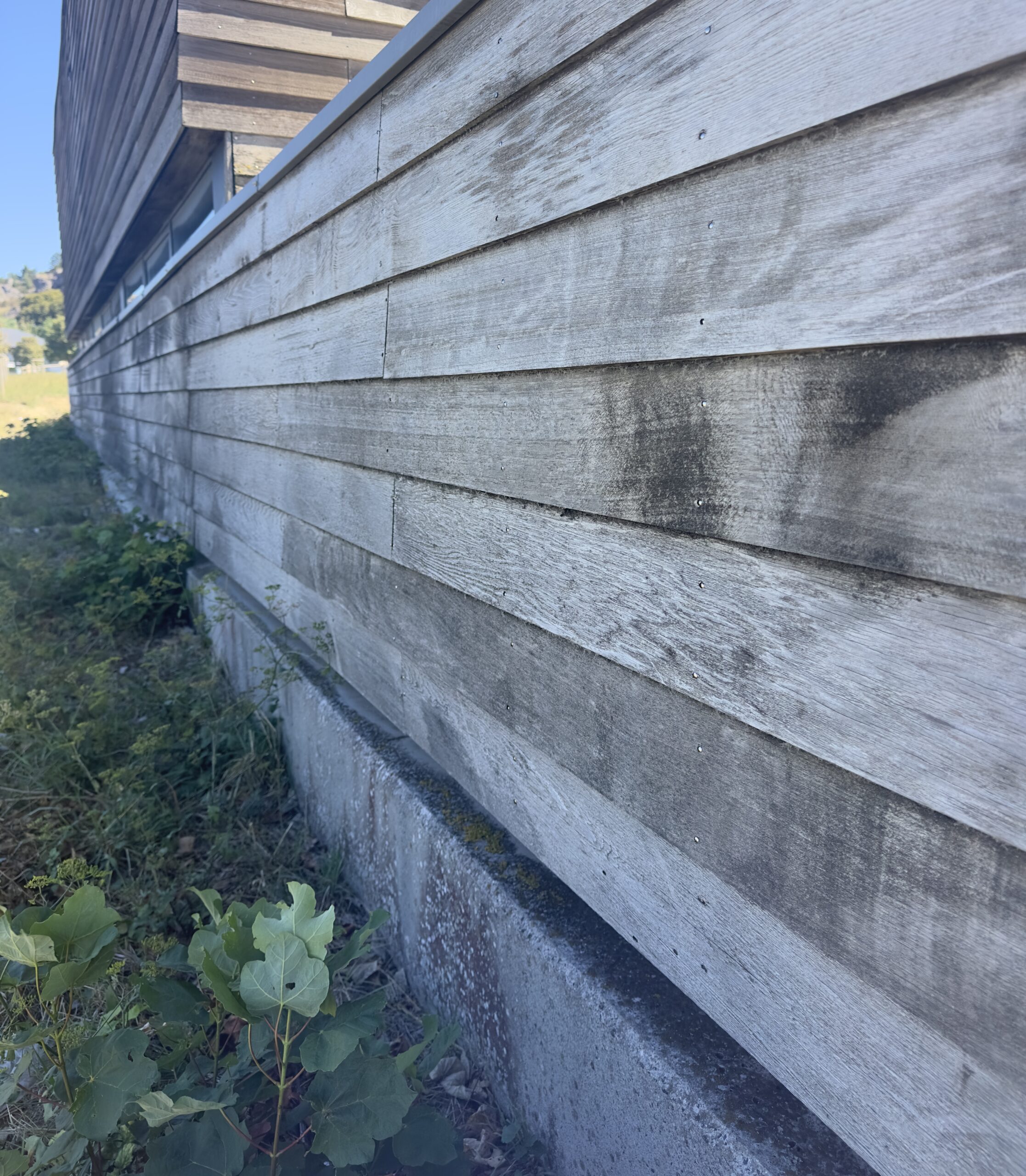 Revestimiento de fachada de madera exterior envejecida y desgastada por el clima, mostrando decoloración y manchas naturales con el paso del tiempo.