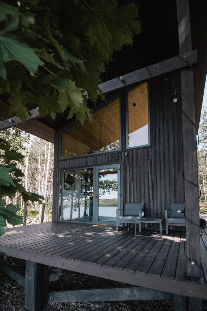 Fachada moderna de una casa de madera Yakisugi con acabado oscuro, grandes ventanales y terraza elevada frente al bosque, mostrando la textura carbonizada y el contraste natural con el entorno verde.