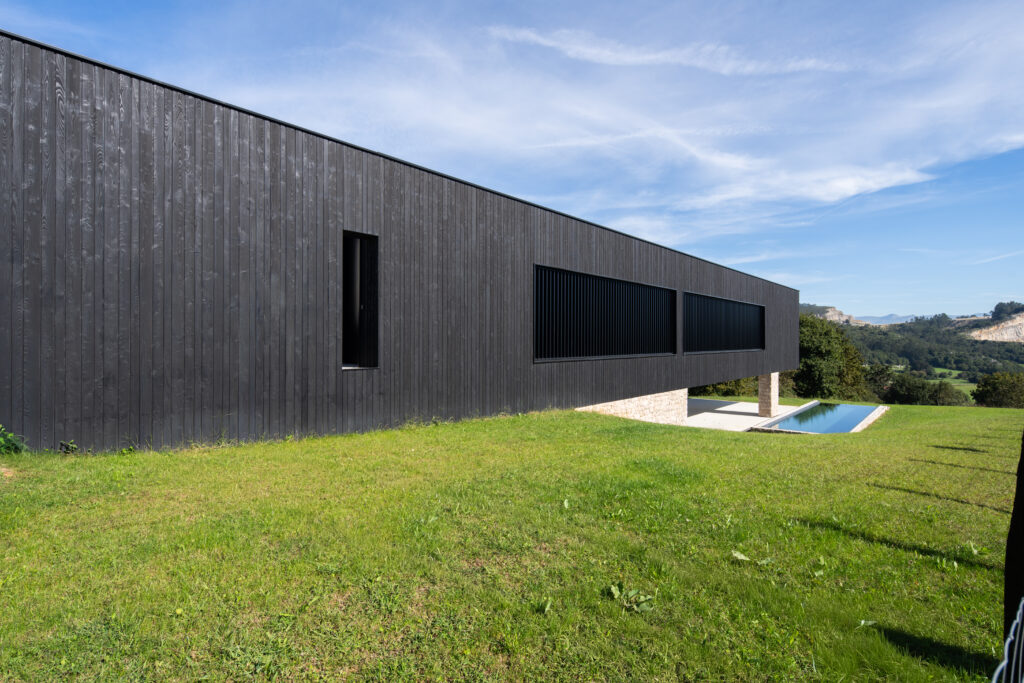 Casa contemporánea de volumen rectangular elevado sobre pilotes de hormigón, revestida en madera yakisugi